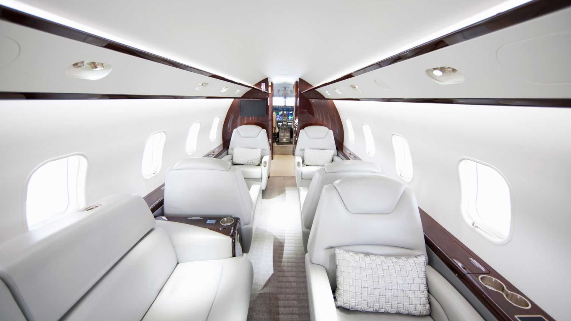 Luxury private jet cabin interior with white leather seats and wood finishes configured for charter flight comfort.